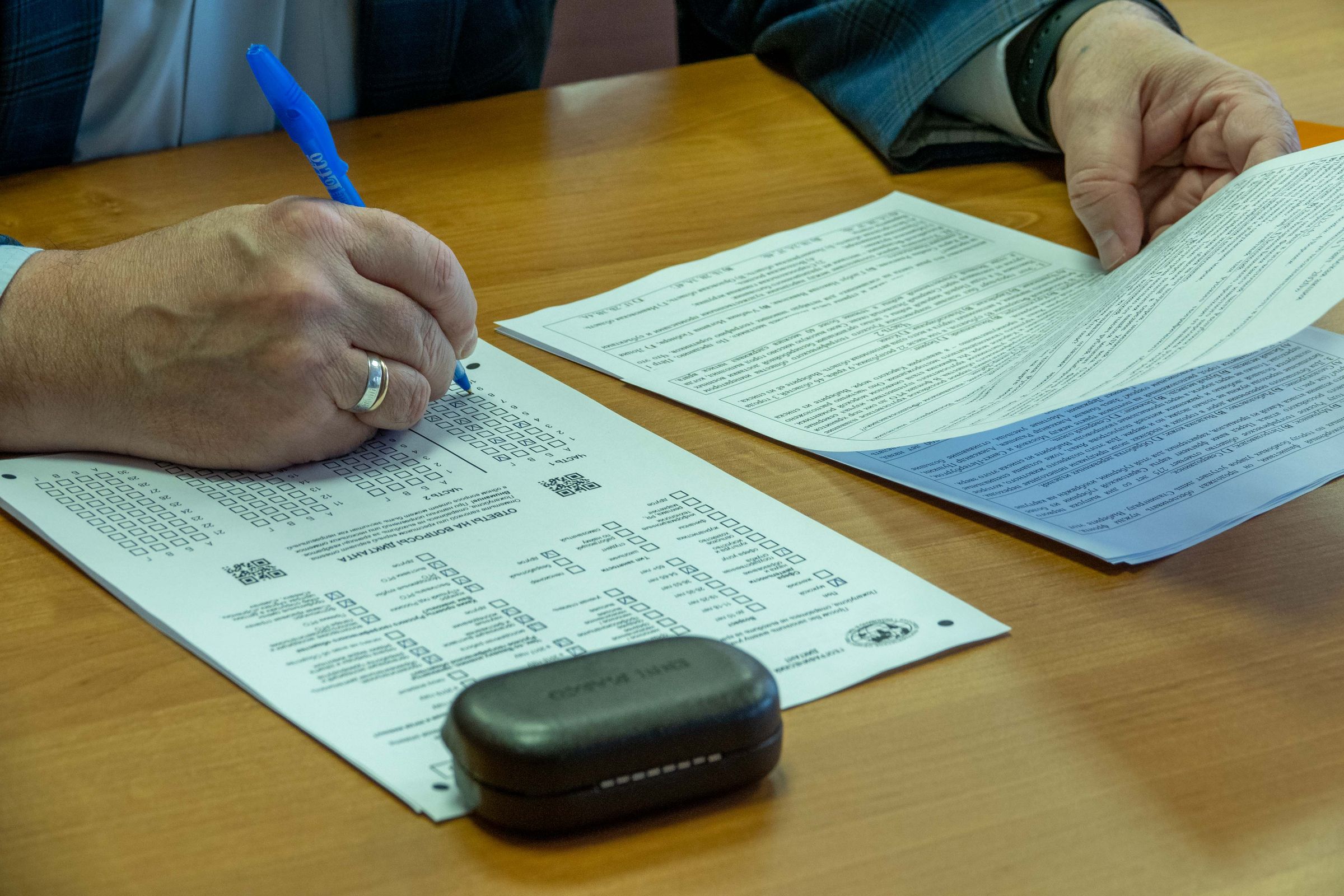 Persoana care completeaza cu pixul un formular oficial pe o masa de lemn.